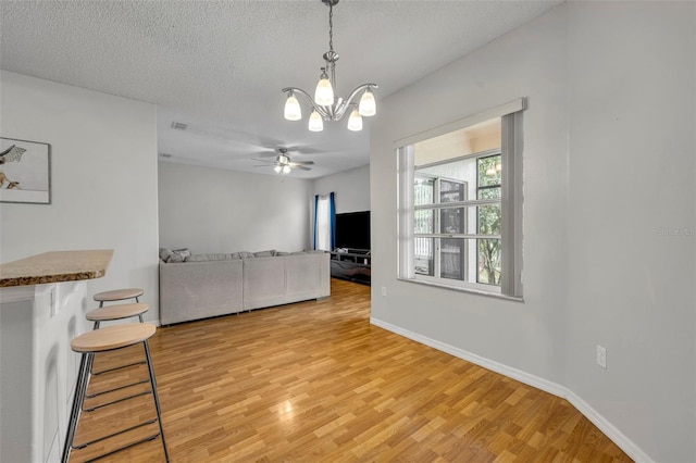 living room with ceiling fan with notable chandelier, a textured ceiling, and light hardwood / wood-style flooring