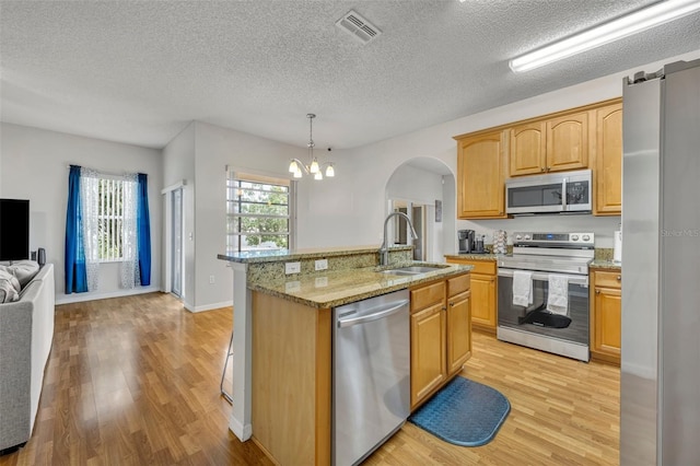 kitchen with decorative light fixtures, sink, light hardwood / wood-style flooring, a kitchen island with sink, and stainless steel appliances