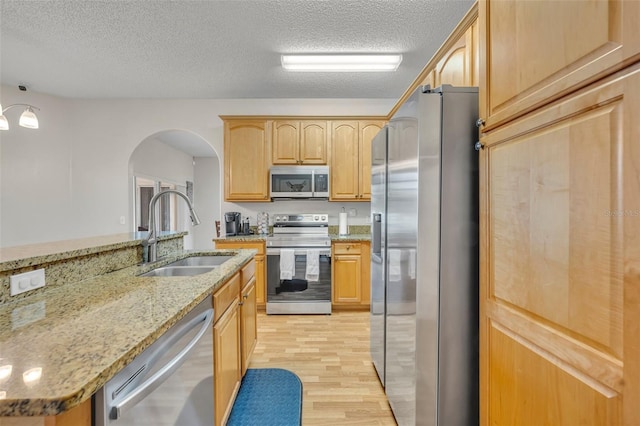 kitchen featuring a textured ceiling, appliances with stainless steel finishes, sink, light stone counters, and light hardwood / wood-style flooring