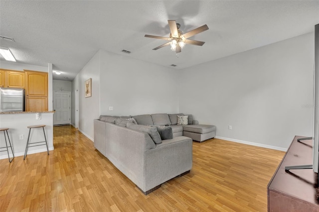 living room with light wood-type flooring, ceiling fan, and a textured ceiling