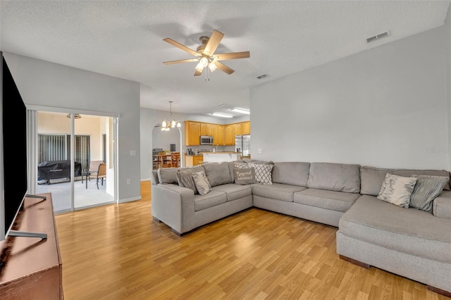 living room with light hardwood / wood-style floors, a textured ceiling, and ceiling fan with notable chandelier