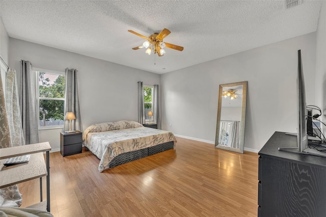 bedroom with ceiling fan, multiple windows, a textured ceiling, and light hardwood / wood-style flooring