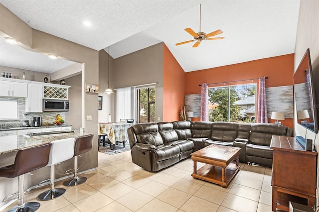 tiled living room with ceiling fan, high vaulted ceiling, and a textured ceiling