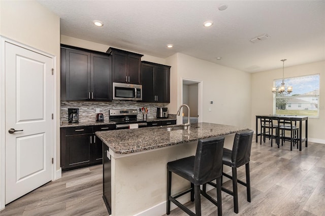 kitchen featuring appliances with stainless steel finishes, sink, dark stone countertops, pendant lighting, and a center island with sink