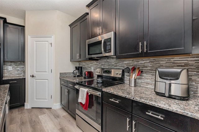 kitchen featuring light stone counters, backsplash, appliances with stainless steel finishes, and light wood-type flooring