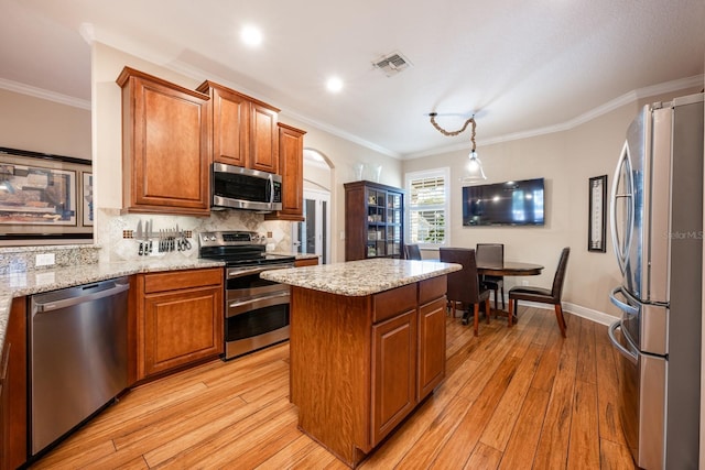 kitchen featuring crown molding, a center island, hanging light fixtures, light hardwood / wood-style flooring, and stainless steel appliances