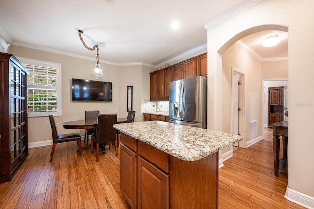 kitchen with light hardwood / wood-style flooring, hanging light fixtures, stainless steel fridge, and a kitchen island