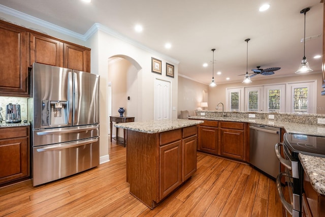 kitchen with light hardwood / wood-style flooring, appliances with stainless steel finishes, light stone counters, a kitchen island, and decorative light fixtures