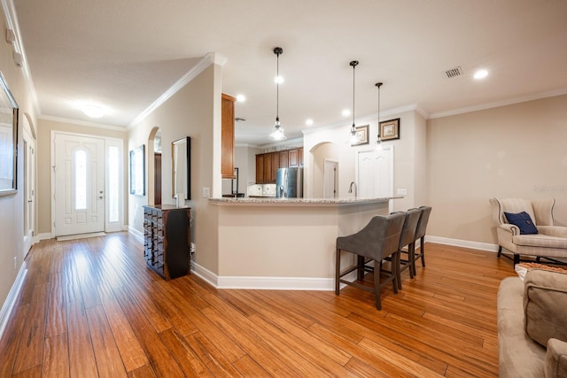 kitchen featuring a kitchen bar, stainless steel fridge with ice dispenser, kitchen peninsula, light stone countertops, and light hardwood / wood-style floors