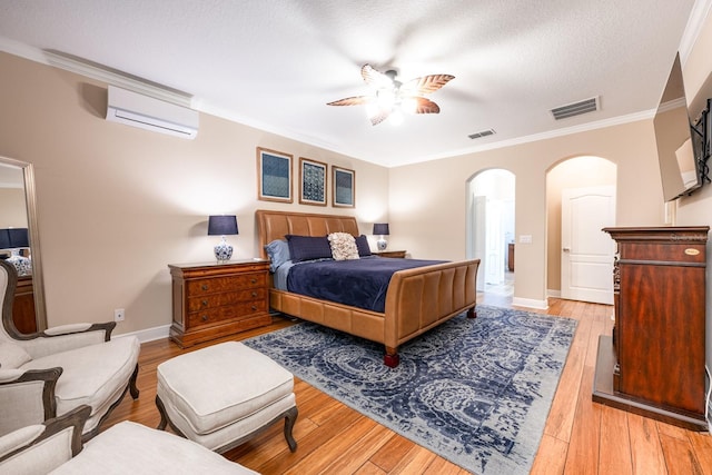 bedroom with an AC wall unit, ceiling fan, crown molding, a textured ceiling, and light hardwood / wood-style flooring