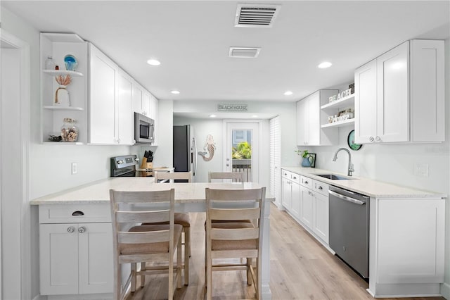 kitchen with sink, appliances with stainless steel finishes, light stone counters, white cabinets, and a kitchen bar