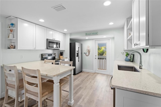 kitchen featuring sink, white cabinets, light stone counters, stainless steel appliances, and light wood-type flooring