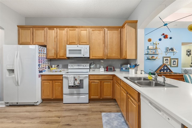 kitchen featuring sink, light wood-type flooring, white appliances, and a textured ceiling