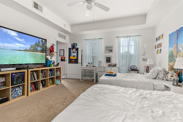 bedroom with ceiling fan, light colored carpet, and a tray ceiling