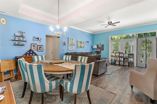 dining space with ornamental molding, a raised ceiling, ceiling fan with notable chandelier, and wood finished floors