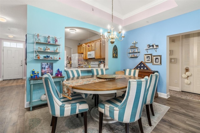 dining area with an inviting chandelier, ornamental molding, wood finished floors, baseboards, and arched walkways