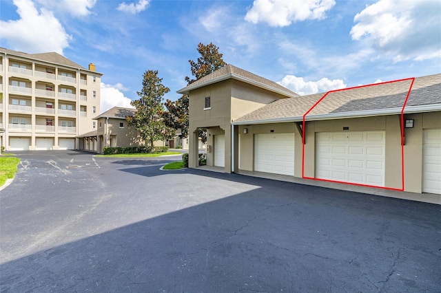 exterior space with roof with shingles, stucco siding, and community garages