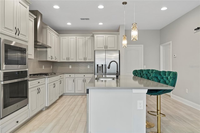 kitchen featuring a kitchen island with sink, backsplash, a kitchen breakfast bar, stainless steel appliances, and wall chimney exhaust hood