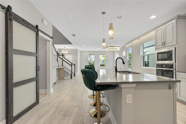 kitchen with built in microwave, an island with sink, sink, oven, and a barn door