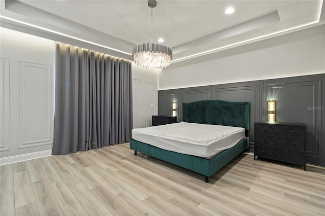 bedroom with an inviting chandelier, light hardwood / wood-style flooring, and a raised ceiling