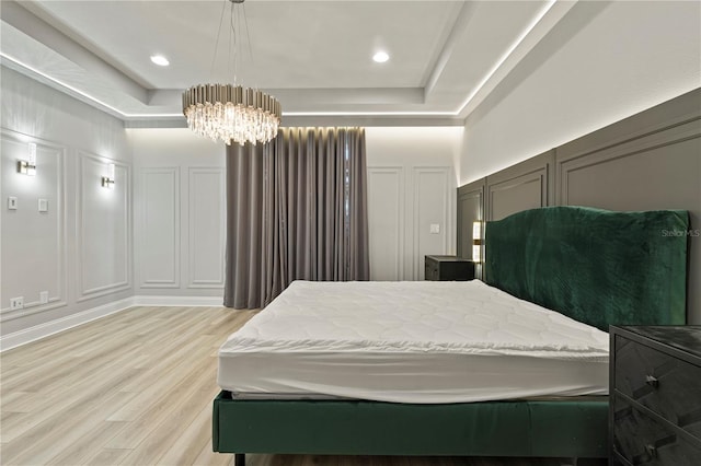 bedroom with a notable chandelier, a tray ceiling, and light hardwood / wood-style flooring