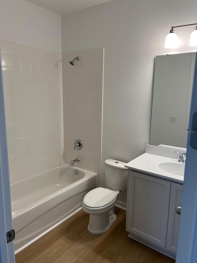 full bathroom with toilet, tiled shower / bath, hardwood / wood-style floors, and vanity