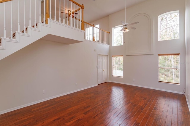 unfurnished living room featuring dark wood-type flooring, a towering ceiling, and ceiling fan