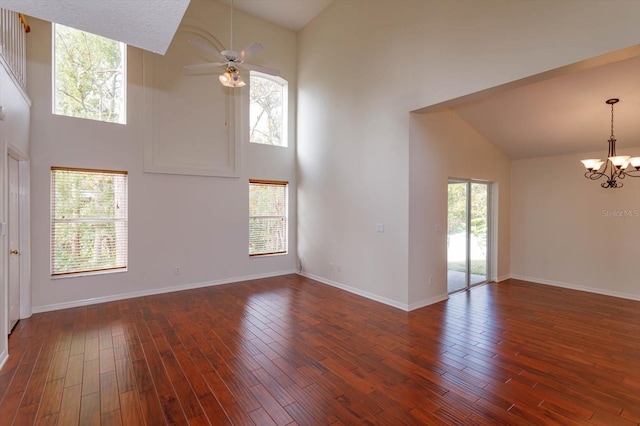 empty room featuring ceiling fan with notable chandelier, a high ceiling, and dark wood-type flooring