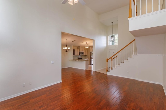 unfurnished living room featuring dark wood-type flooring, a high ceiling, and ceiling fan with notable chandelier