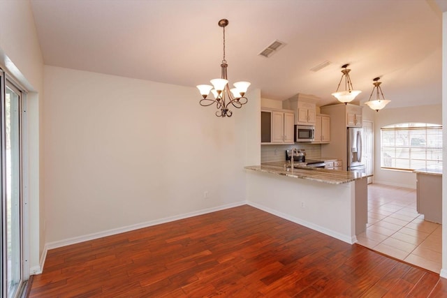 kitchen with appliances with stainless steel finishes, tasteful backsplash, light hardwood / wood-style floors, hanging light fixtures, and kitchen peninsula