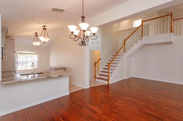 kitchen with wood-type flooring, stainless steel fridge, decorative light fixtures, sink, and light stone counters