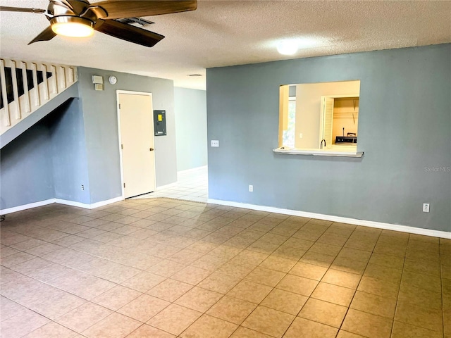 tiled empty room with ceiling fan, electric panel, and a textured ceiling