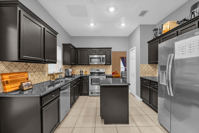 kitchen with sink, light tile patterned floors, appliances with stainless steel finishes, dark stone countertops, and a kitchen island