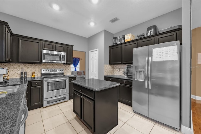 kitchen featuring a kitchen island, tasteful backsplash, dark stone countertops, light tile patterned floors, and stainless steel appliances