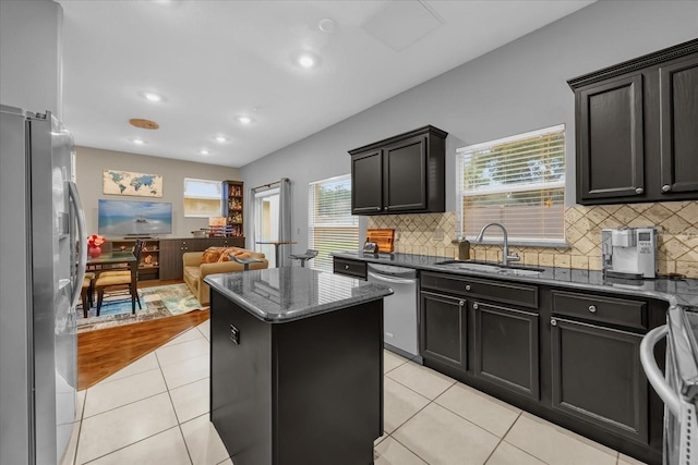 kitchen with appliances with stainless steel finishes, sink, dark stone countertops, a center island, and light tile patterned floors