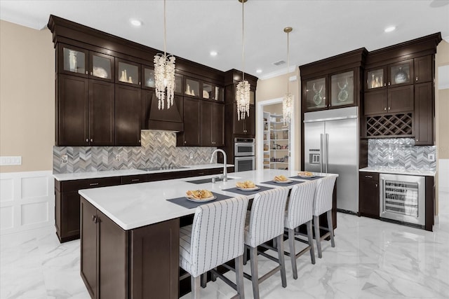 kitchen with wine cooler, hanging light fixtures, appliances with stainless steel finishes, sink, and an island with sink