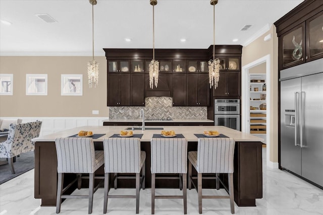 kitchen featuring pendant lighting, appliances with stainless steel finishes, sink, a center island with sink, and dark brown cabinetry