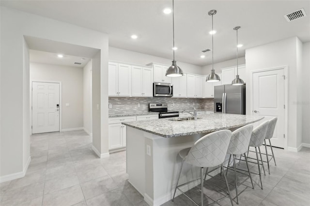 kitchen with appliances with stainless steel finishes, sink, white cabinets, a kitchen island with sink, and light stone counters