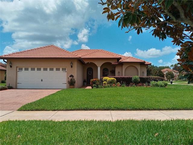 mediterranean / spanish home with decorative driveway, a tile roof, stucco siding, a garage, and a front lawn