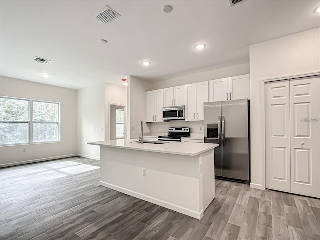 kitchen with appliances with stainless steel finishes, white cabinetry, sink, light hardwood / wood-style flooring, and a center island with sink