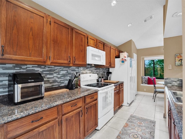 kitchen with light tile patterned flooring, backsplash, white appliances, and dark stone countertops