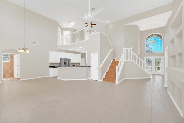 unfurnished living room featuring a towering ceiling, french doors, ceiling fan with notable chandelier, and light tile patterned floors