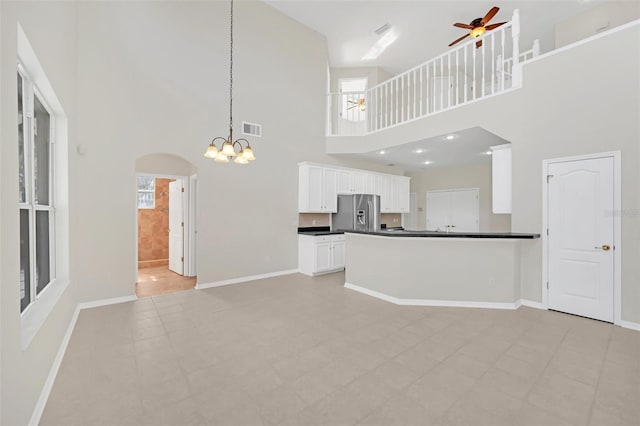 unfurnished living room with ceiling fan with notable chandelier, a towering ceiling, and light tile patterned floors