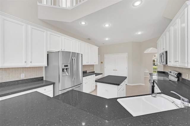 kitchen with a center island, white cabinetry, stainless steel appliances, dark stone countertops, and sink