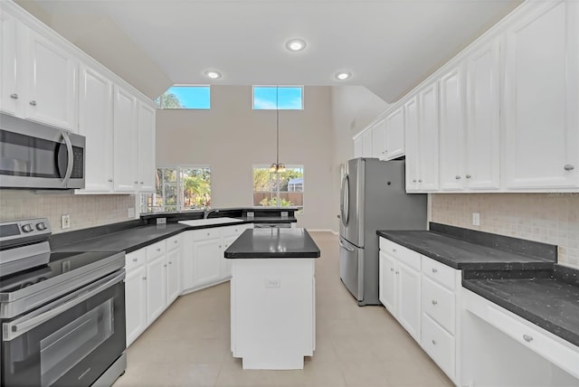 kitchen with pendant lighting, appliances with stainless steel finishes, white cabinets, tasteful backsplash, and a kitchen island