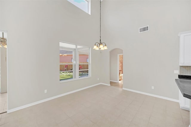 unfurnished dining area featuring a notable chandelier, a towering ceiling, and light tile patterned floors