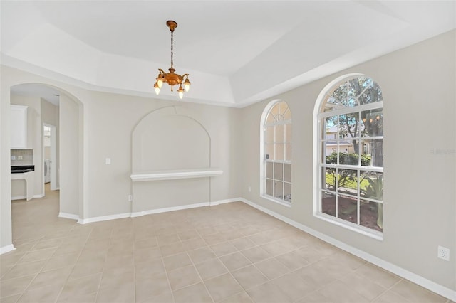 spare room with an inviting chandelier, light tile patterned floors, and a tray ceiling