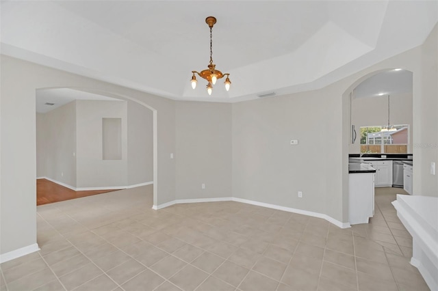 tiled spare room with a raised ceiling and an inviting chandelier