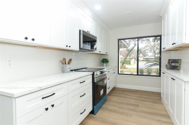 kitchen with light stone countertops, appliances with stainless steel finishes, white cabinets, and light wood-type flooring