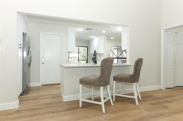 kitchen with a breakfast bar, stainless steel refrigerator, white cabinetry, kitchen peninsula, and light wood-type flooring